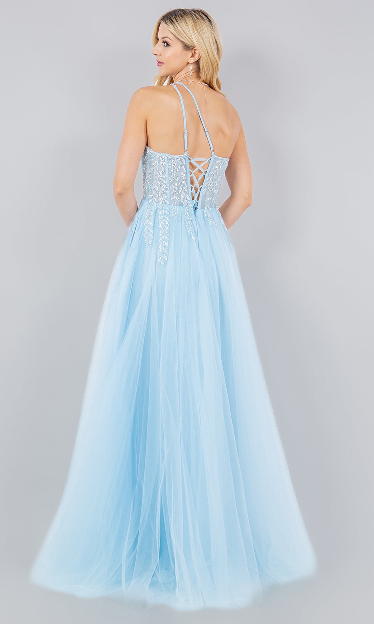 A woman stands with her back to the camera in the Cinderella Couture 8118J, a light blue pastel tulle prom dress featuring thin straps and a lace-up back.